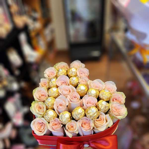 Pink roses and gold-wrapped chocolates in a red heart-shaped box with a ribbon