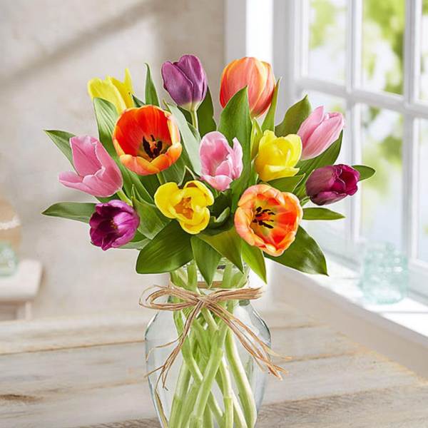 Colorful tulips arranged in a clear glass vase with a raffia bow.