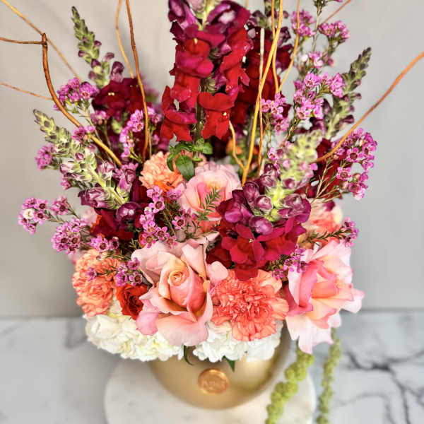 Tall floral arrangement with pink roses and magenta snapdragons in a gold vase
