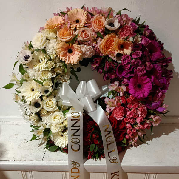 Heart-shaped floral wreath with pink, white, and peach blooms and a white ribbon bow