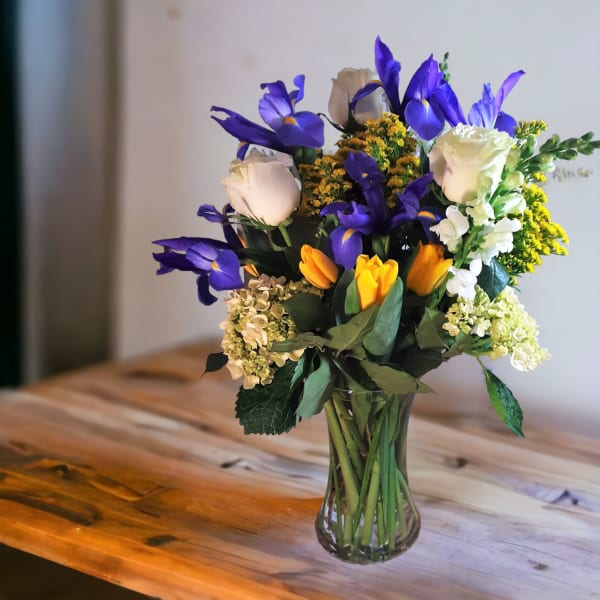 Bouquet of purple irises, white roses, and yellow flowers in a glass vase