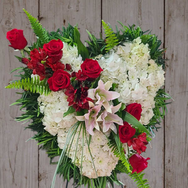 Heart-shaped floral wreath with red roses and white blooms on a stand