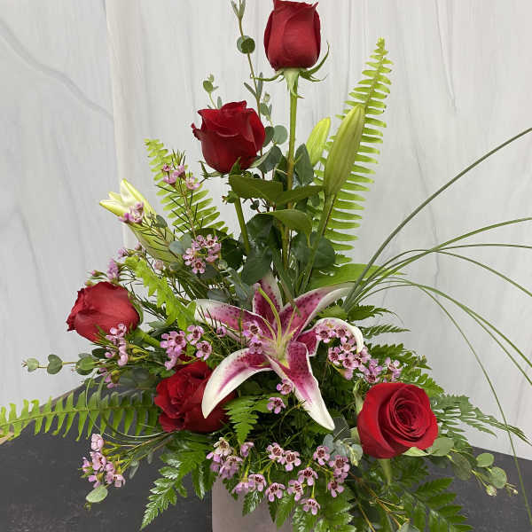 Tall arrangement of red roses and a pink stargazer lily in a square vase