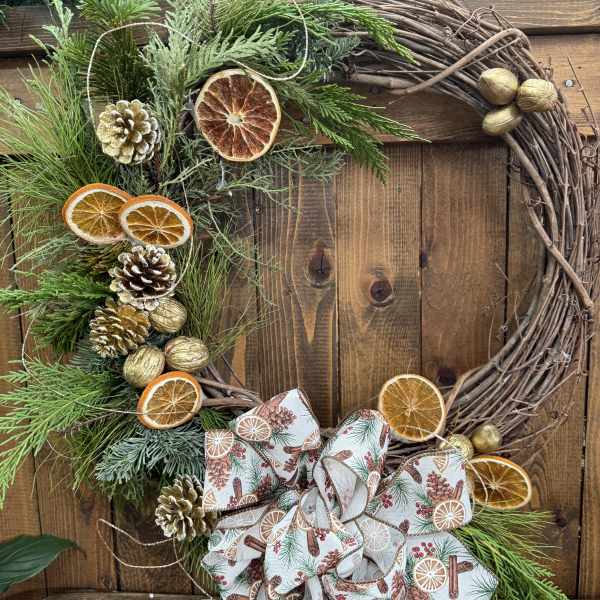 Holiday wreath with pine, dried citrus slices, pinecones, and a patterned bow