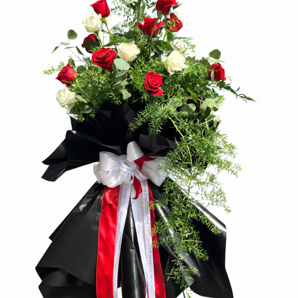 Tall standing arrangement of red and white roses with black wrap and ribbons