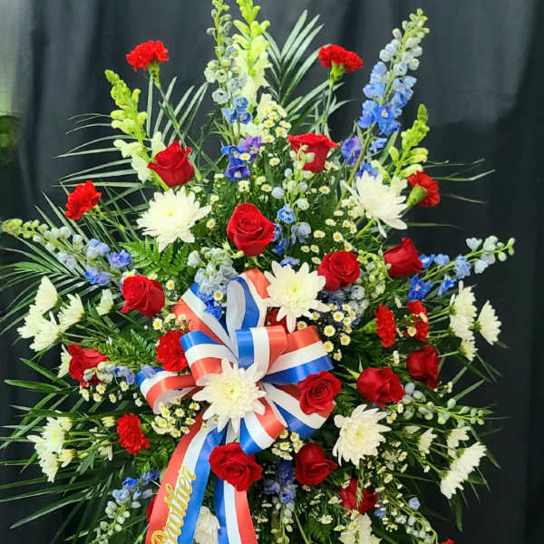 Large standing floral spray with red roses, white daisies, and blue flowers