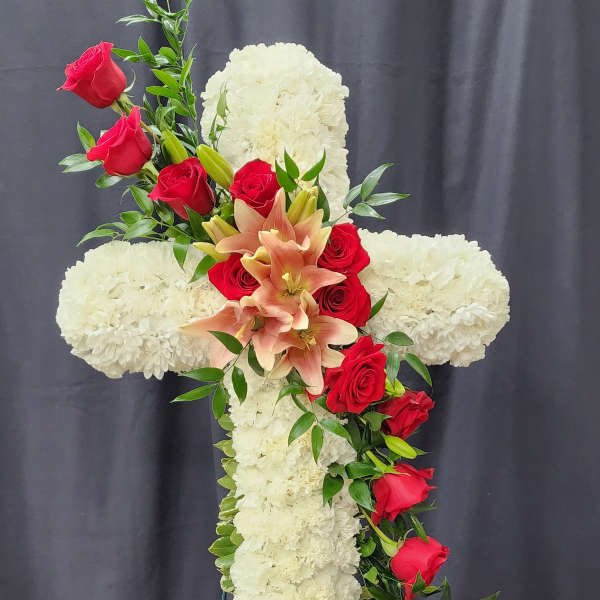 White floral cross with red roses and peach lilies on a stand
