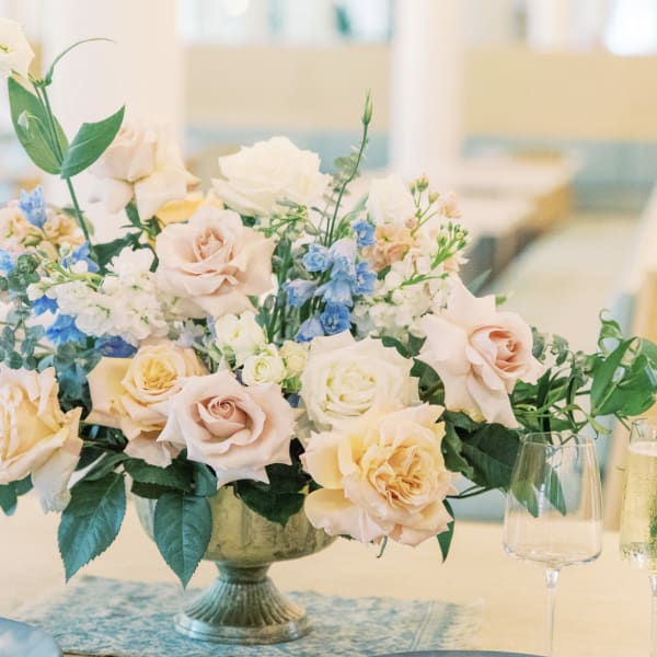Pastel rose centerpiece in a pedestal vase with blue and white flowers