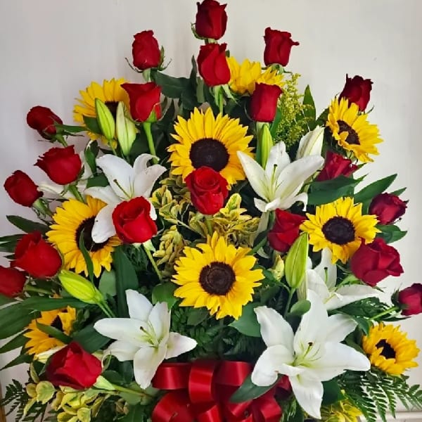 Red roses, white lilies, and yellow sunflowers in a white basket with a red ribbon