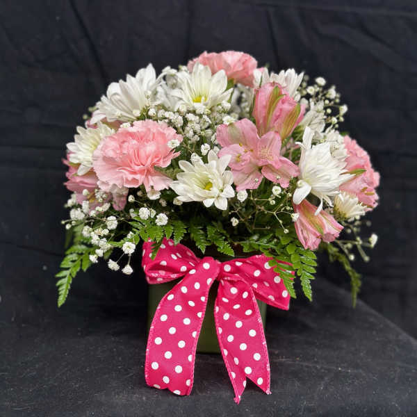 Pink and white flowers in a green vase with a polka-dot ribbon