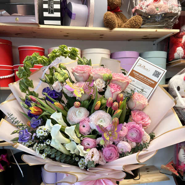 Large pastel bouquet with pink, purple, and white flowers wrapped in blush paper