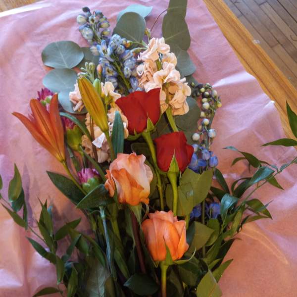 Mixed bouquet with roses, lilies, and blue flowers on pink paper