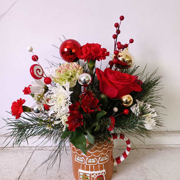 Red and white floral arrangement in a gingerbread mug with holiday ornaments