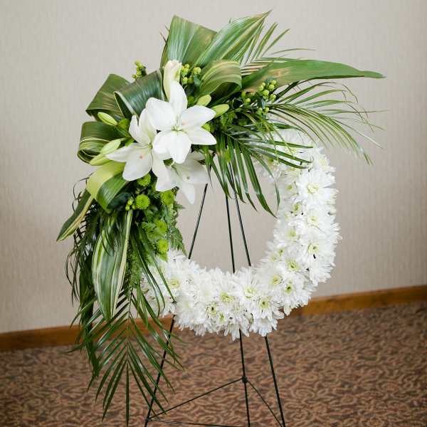 White floral funeral wreath on a black stand with lilies and daisies