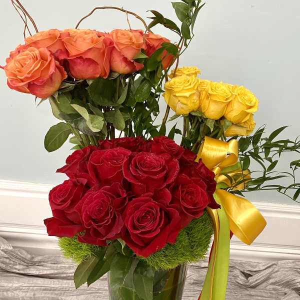 Three rose bouquets in a glass vase with yellow ribbon