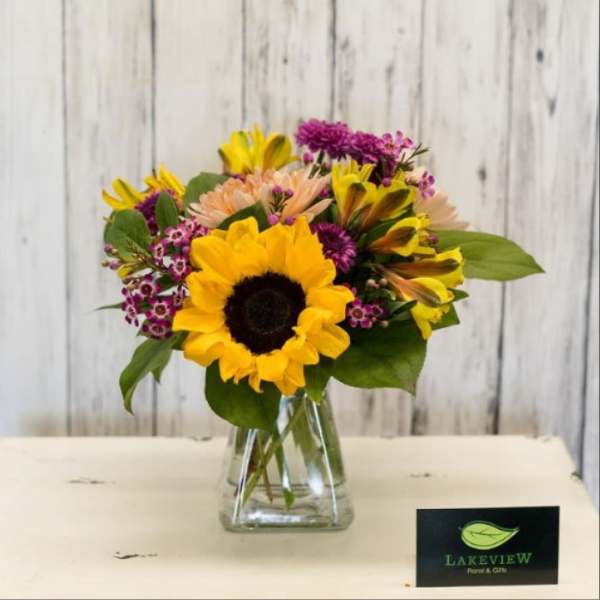 Sunflower bouquet with purple and peach flowers in a clear glass vase
