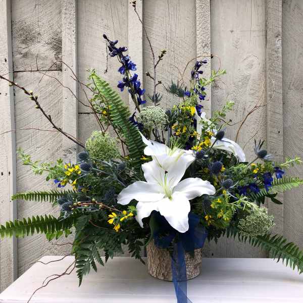 White lilies in a rustic container with blue and yellow flowers