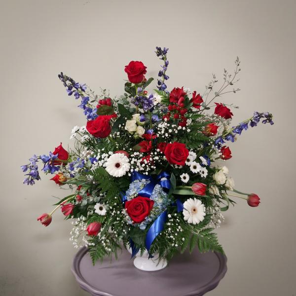 Large bouquet of red roses, white daisies, and blue flowers in a white vase