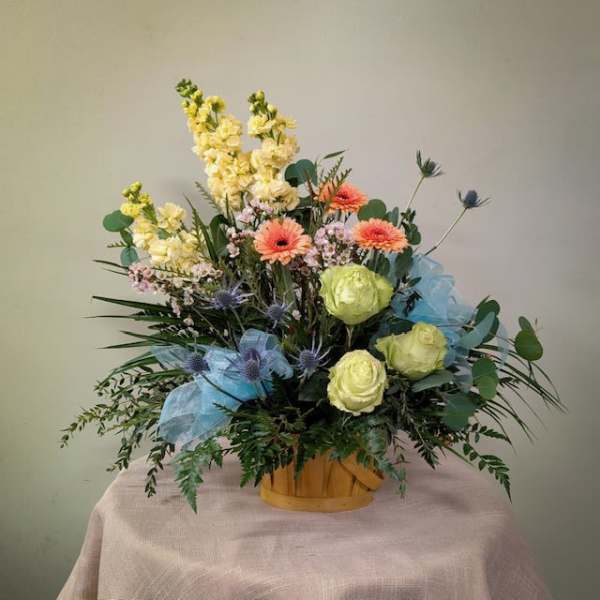 Mixed bouquet in a wooden basket with pale yellow, peach, and blue flowers