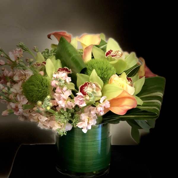 Bouquet of calla lilies, orchids, and pink flowers in a green glass vase