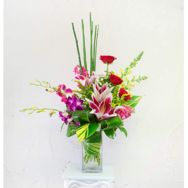 Tropical bouquet with red roses, pink lilies, and purple orchids in a glass vase