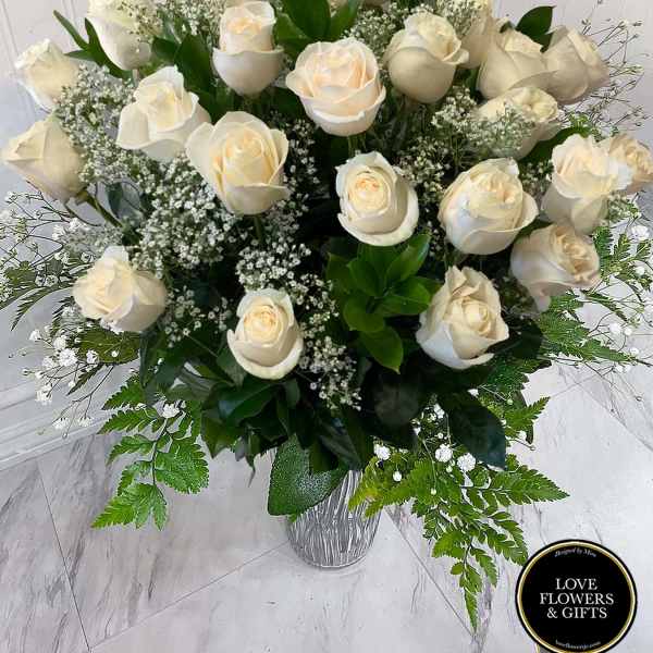 Tall arrangement of white roses and baby’s breath in a clear glass vase