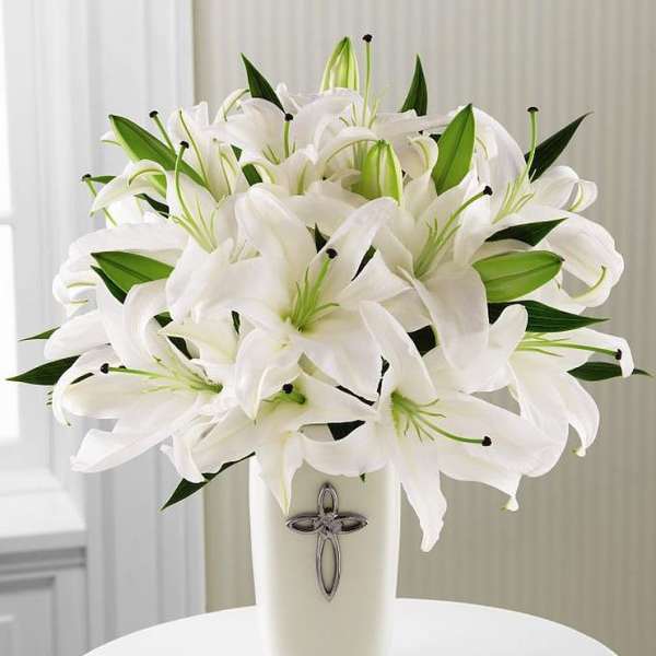 White lilies arranged in a tall vase with a cross emblem