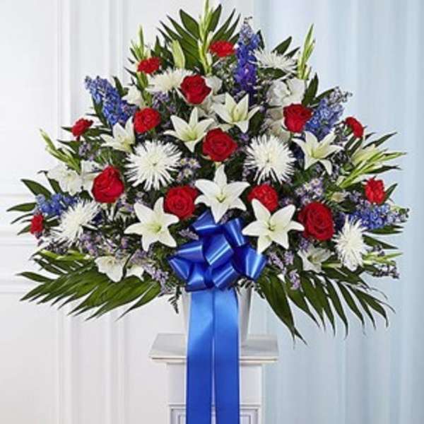 Standing floral spray with red roses, white lilies, and blue accents on a pedestal