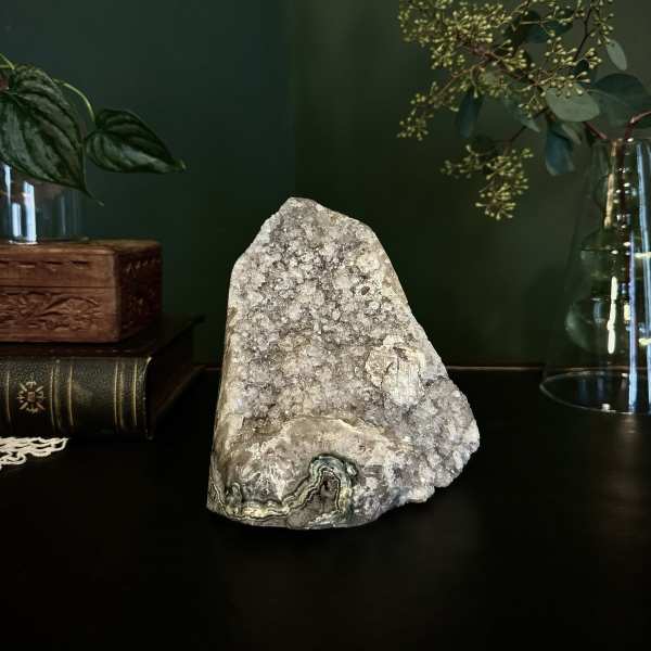 Crystal geode on a dark surface with glass vases and greenery