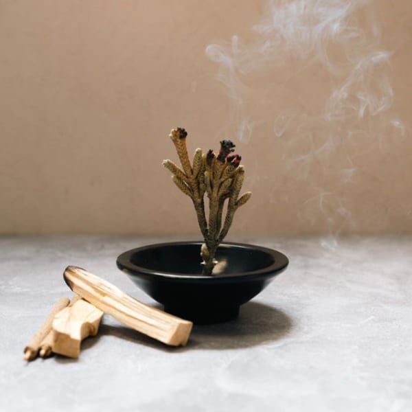 Burning incense sticks in a black bowl with smoke rising