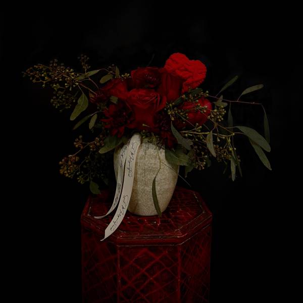 Red rose arrangement in a textured vase on a red pedestal