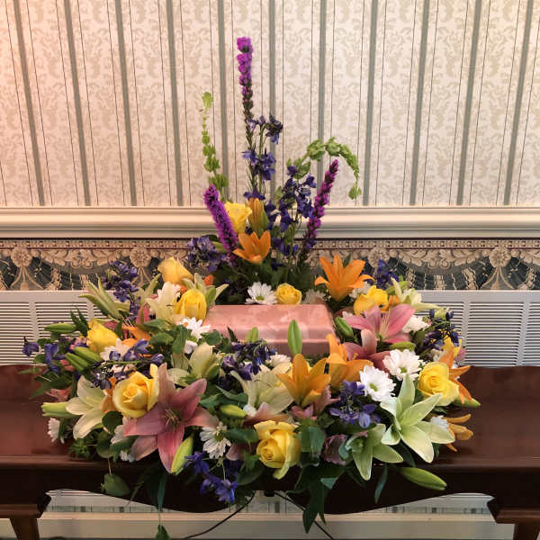 Large floral casket spray with lilies, roses, and purple accents