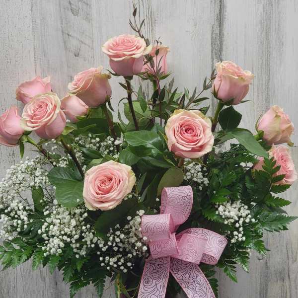 Pink roses arranged in a dark glass vase with a pink ribbon