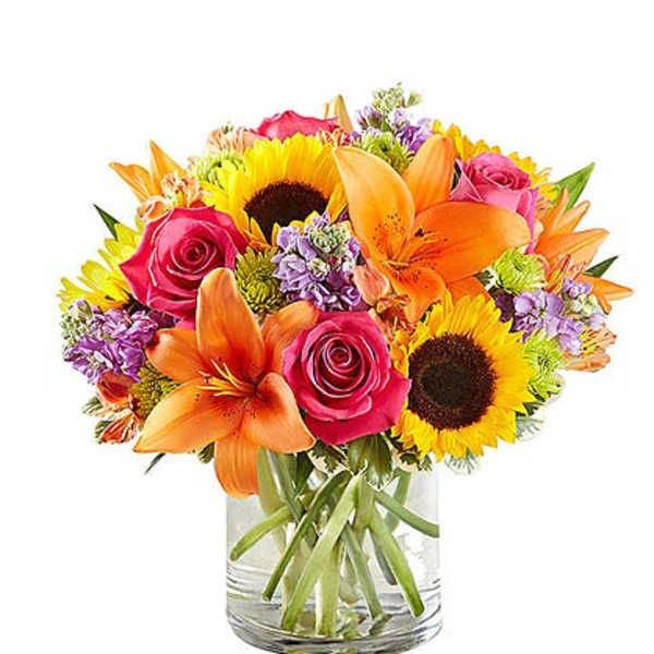 Mixed bouquet of sunflowers, orange lilies, and pink roses in a glass vase