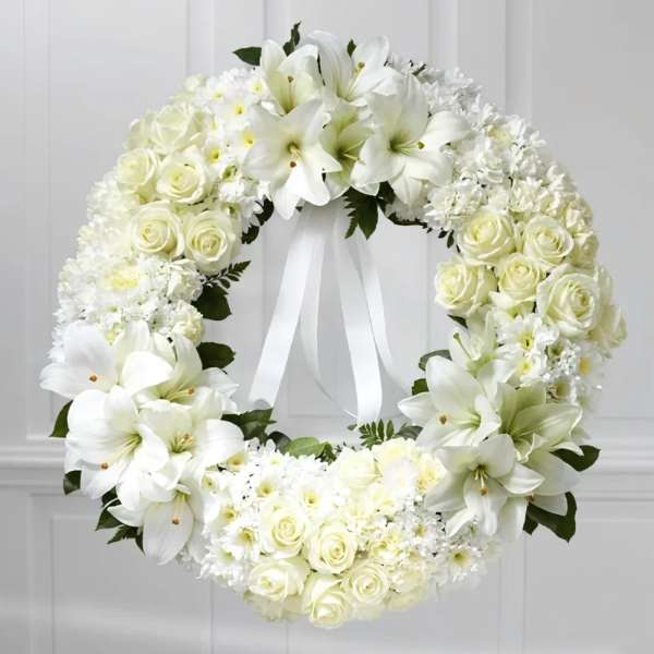 White floral wreath with roses and lilies and a ribbon bow