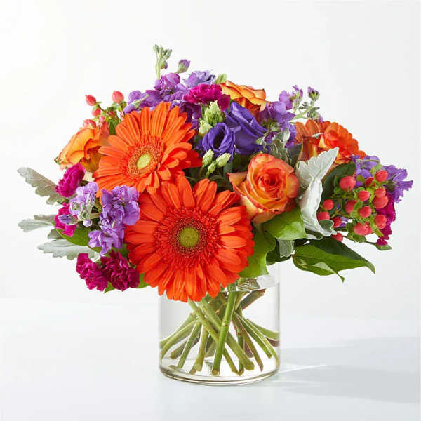 Bright mixed bouquet of orange, purple, and pink flowers in a clear glass vase
