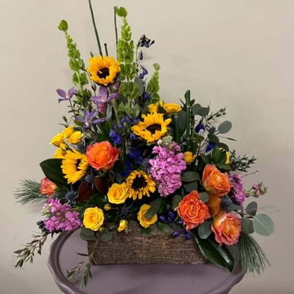 Mixed bouquet with sunflowers, roses, and purple blooms in a rustic basket