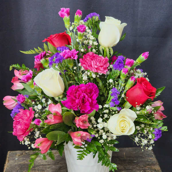 Mixed bouquet of roses, carnations, and purple filler in a white vase