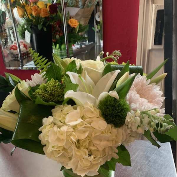 White floral arrangement in a glass vase with green accents