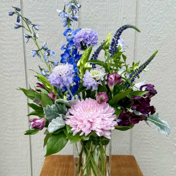 Mixed bouquet of pink, purple, and blue flowers in a clear glass vase