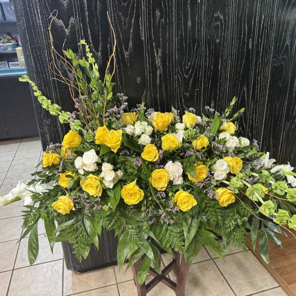 Yellow and white rose arrangement with greenery on a stand