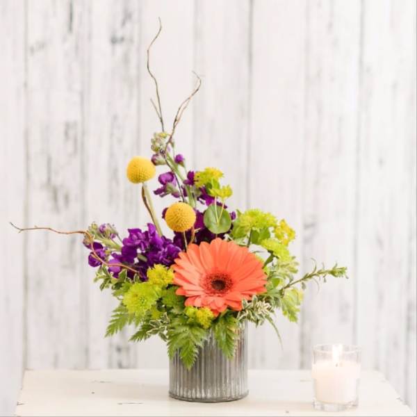 Colorful flower arrangement in a ribbed glass vase beside a white candle.