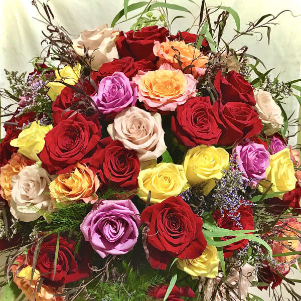 Large arrangement of mixed red, yellow, peach, and lavender roses in a rounded design
