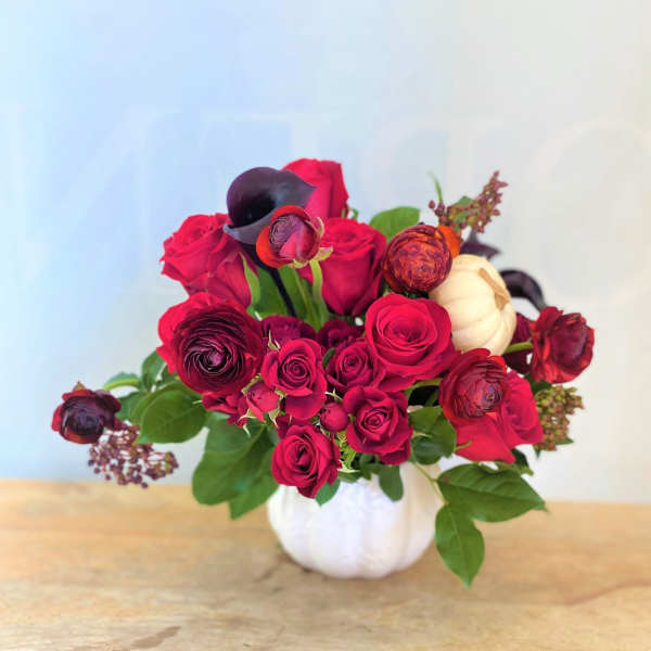 Red roses and dark ranunculus in a white pumpkin vase