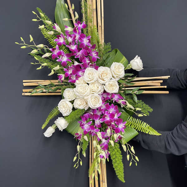 Cross-shaped floral arrangement with white roses and purple orchids on bamboo