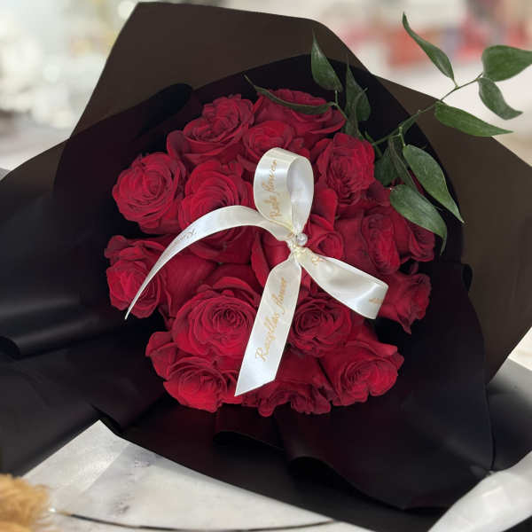Bouquet of red roses wrapped in black paper with a white ribbon