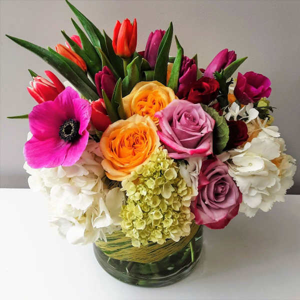 Colorful bouquet of roses, tulips, anemone, and hydrangea in a glass vase