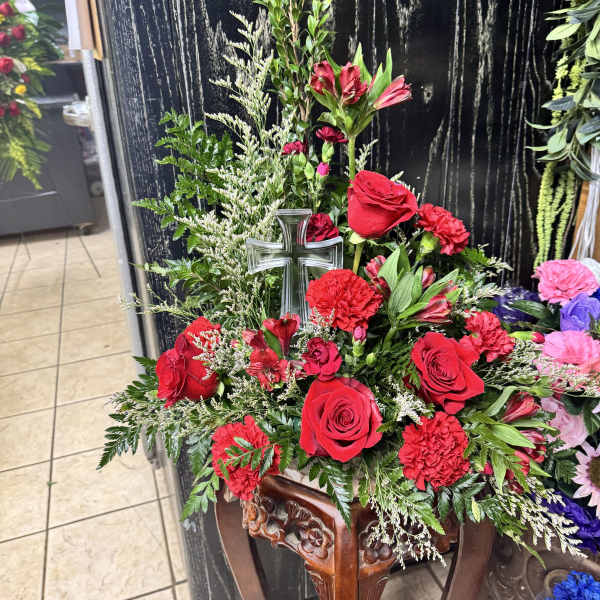 Red roses and carnations arranged with a glass cross in a wooden stand