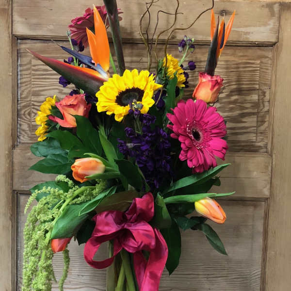 Tall tropical bouquet with sunflowers, gerbera daisies, tulips, and bird of paradise in a glass vase