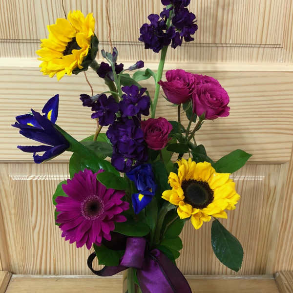 Colorful mixed bouquet in a clear glass vase with a purple ribbon